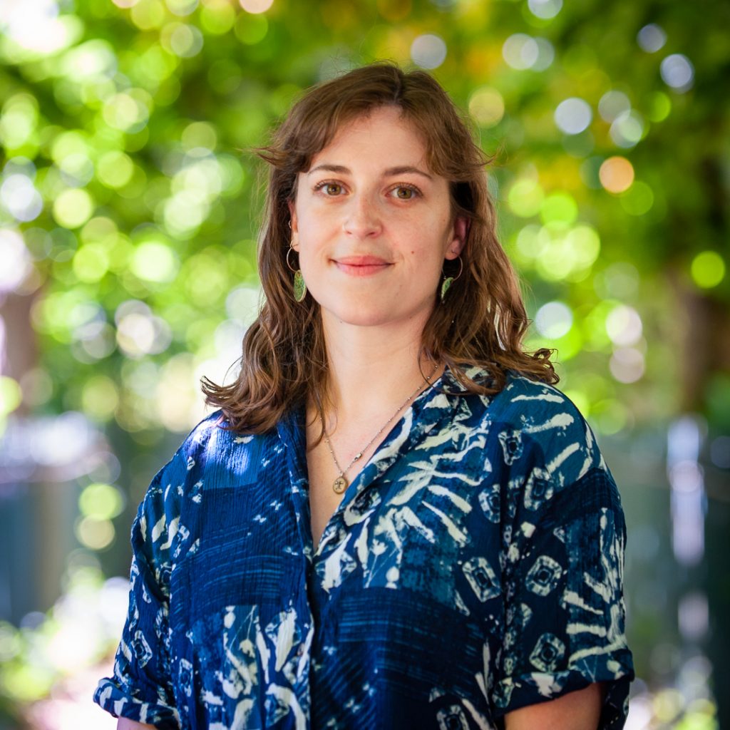 Alice - woman in her 30s with brown wavy hair, wearing a blue and white casual shirt.